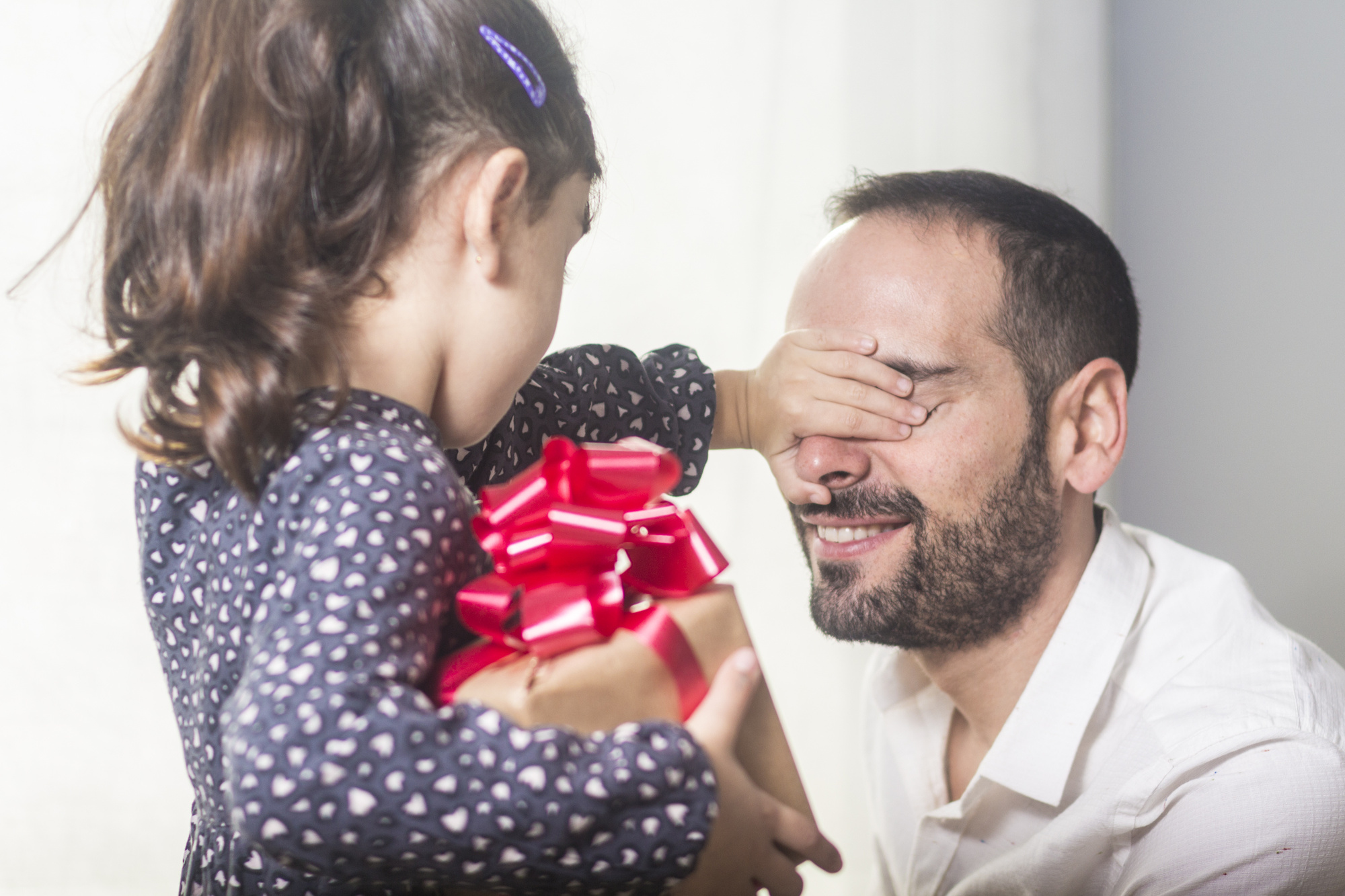 Girl hiding gift while covering happy father eyes at Father day